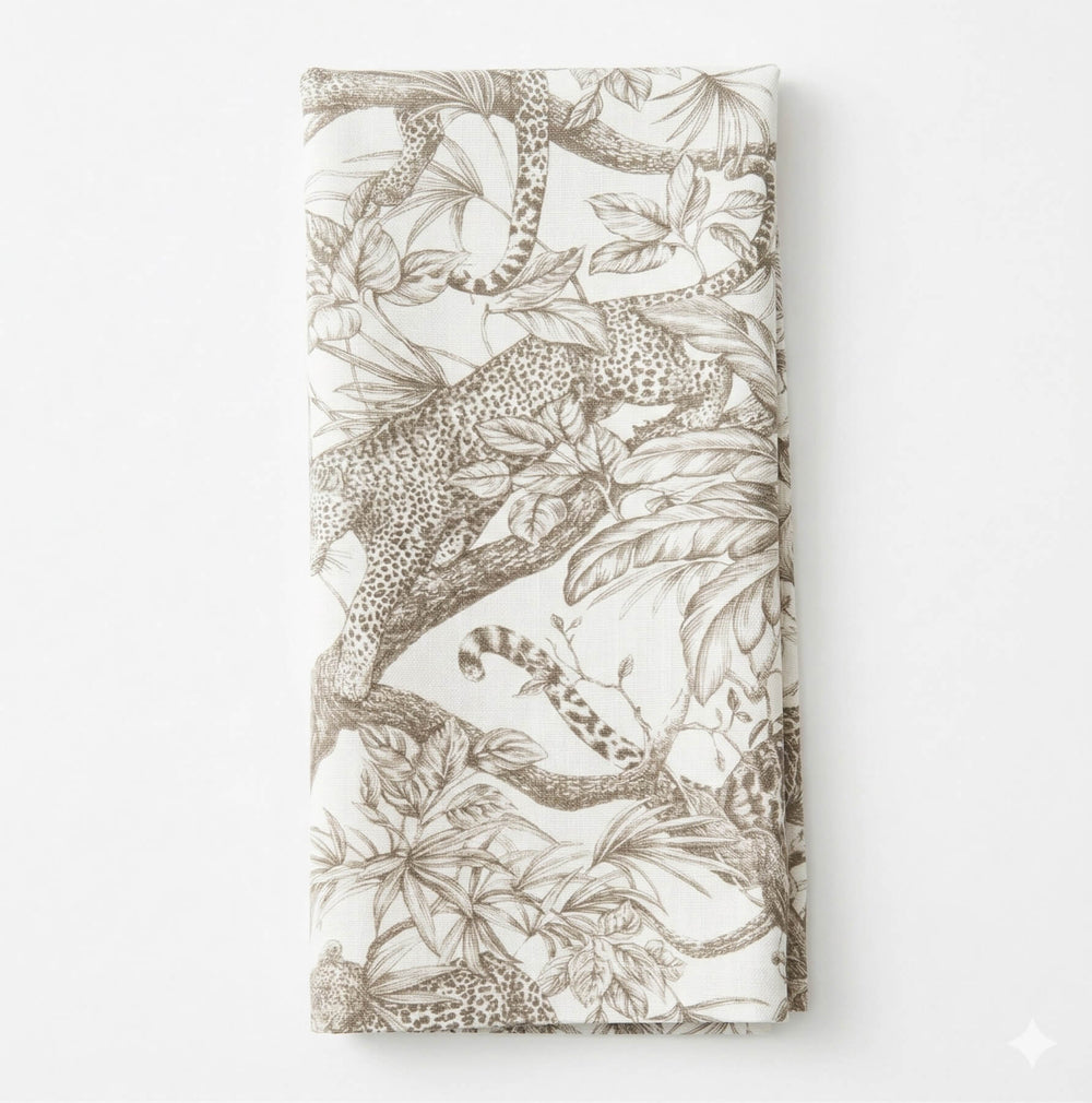 A close-up of a table draped in Leonard Mono Linen, showcasing monochrome linen with artistic black-and-white leopard jungle motifs and detailed foliage.