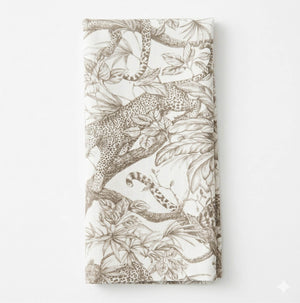 A folded white Leonard Mono Linen napkin with a detailed brown leopard and leafy branch design, capturing jungle motifs and exotic elegance.