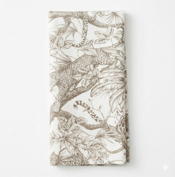 A folded white Leonard Mono Linen napkin with a detailed brown leopard and leafy branch design, capturing jungle motifs and exotic elegance.
