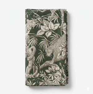The Leonard Olive Linen napkin features detailed leopard motifs, tree branches, and tropical leaves in beige and off-white on a folded olive linen background.