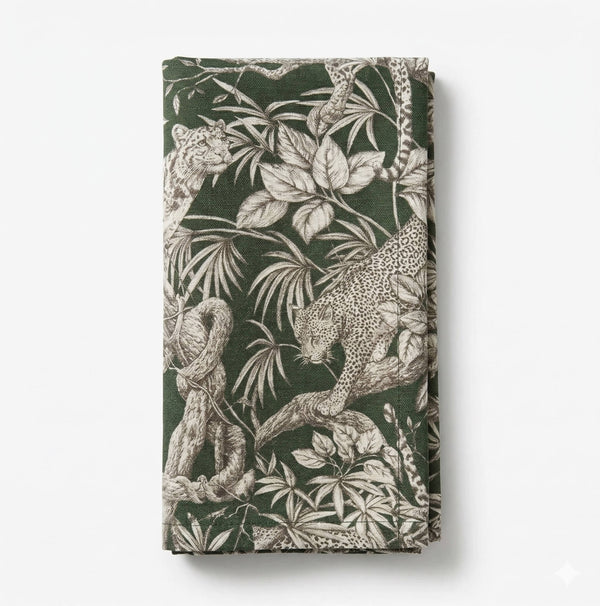 The Leonard Olive Linen napkin features detailed leopard motifs, tree branches, and tropical leaves in beige and off-white on a folded olive linen background.