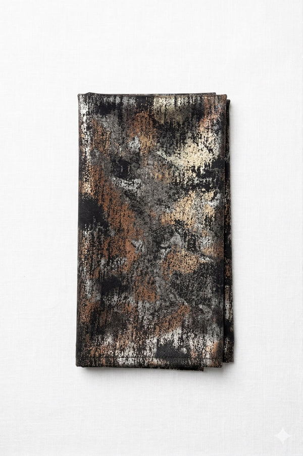 A folded Luna Linen napkin with an abstract pattern in black, brown, tan, and gray adds celestial elegance to your table, displayed on a white background.
