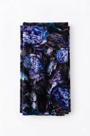 A folded rectangular Seraphina Linen piece features vibrant purple, blue, and green florals on white—ideal as a luxurious table linen.