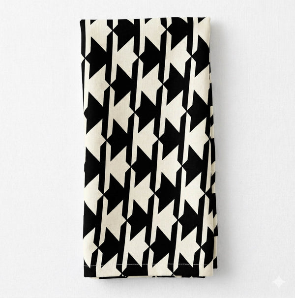 The Stella Linen napkin, showcasing a bold black and white houndstooth pattern, is neatly folded and displayed on a plain white background.