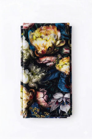 The Vivienne Linen is a neatly folded fabric napkin featuring a vibrant, detailed floral pattern in various colors, reminiscent of elegant table linens, set against a white background.