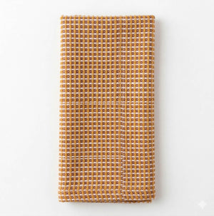 A folded, textured kitchen towel called "Waffle Burnt Orange Linen" is shown on a plain white background. It features a distinctive burnt orange and white checkered waffle pattern.