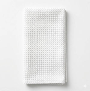 The Waffle Ivory Linen towel, featuring a textured, waffle-like pattern, is neatly folded on a white surface, evoking an elegant and refined look.