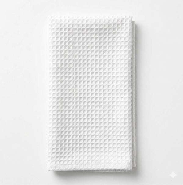 The Waffle Ivory Linen towel, featuring a textured, waffle-like pattern, is neatly folded on a white surface, evoking an elegant and refined look.