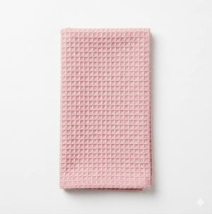 The Waffle Pink Linen towel, featuring a neat fold and waffle pattern, rests elegantly on a white surface.
