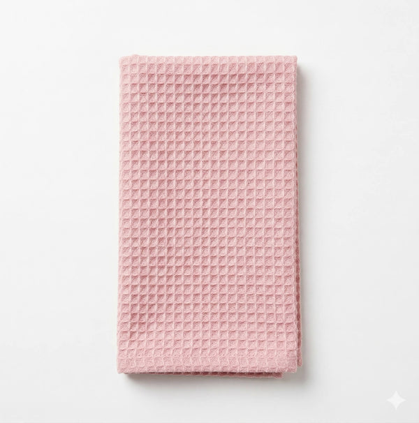 The Waffle Pink Linen towel, featuring a neat fold and waffle pattern, rests elegantly on a white surface.